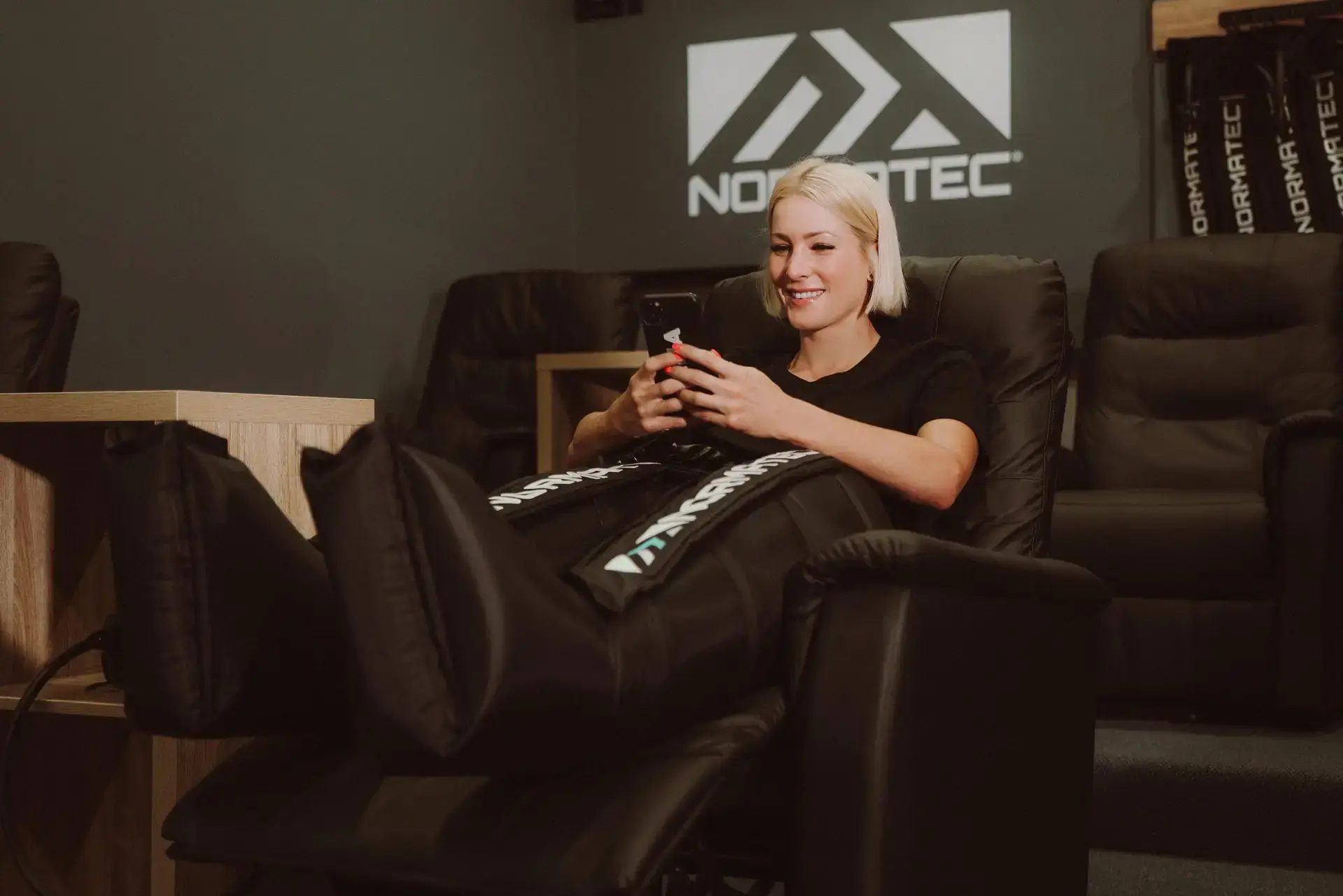 Woman using Normatec compression therapy tools in recovery lounge?